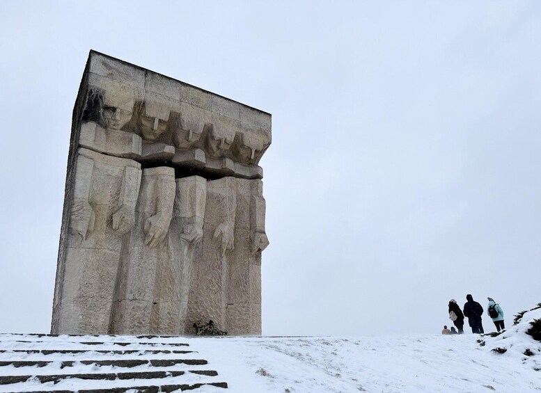 A large, monolithic structure with carved figures, set against a snowy landscape with a few people in the background. 1