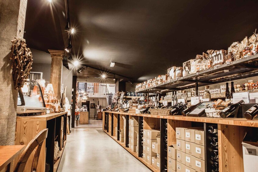 A store with wooden shelves stocked with boxes and bottles, a staircase in the background, and a rustic decor with a tree trunk. 2