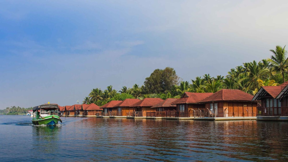 A row of wooden houses with red roofs on stilts over water, a green boat in the foreground, and palm trees in the background. 3