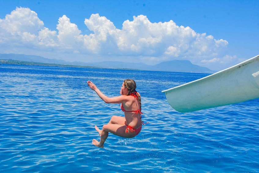 Une personne portant un bikini rouge, assise sur un bateau dans l’océan, avec un ciel dégagé et des montagnes en arrière-plan. 5