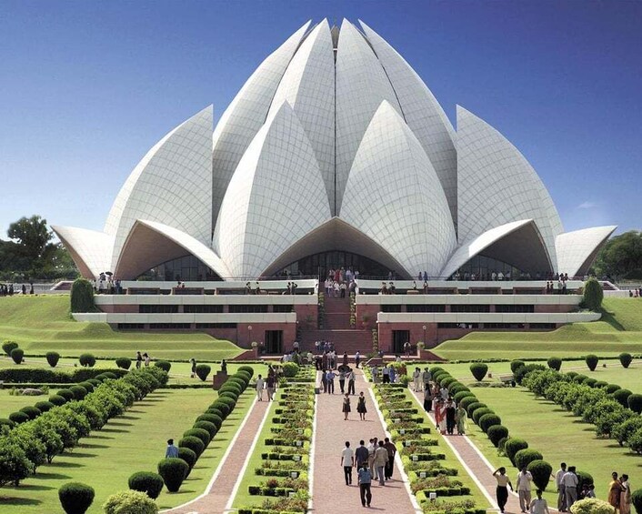 Un grand bâtiment de forme circulaire, blanc, évoquant une fleur de lotus, avec une entrée centrale et un jardin qui l’entoure. 1