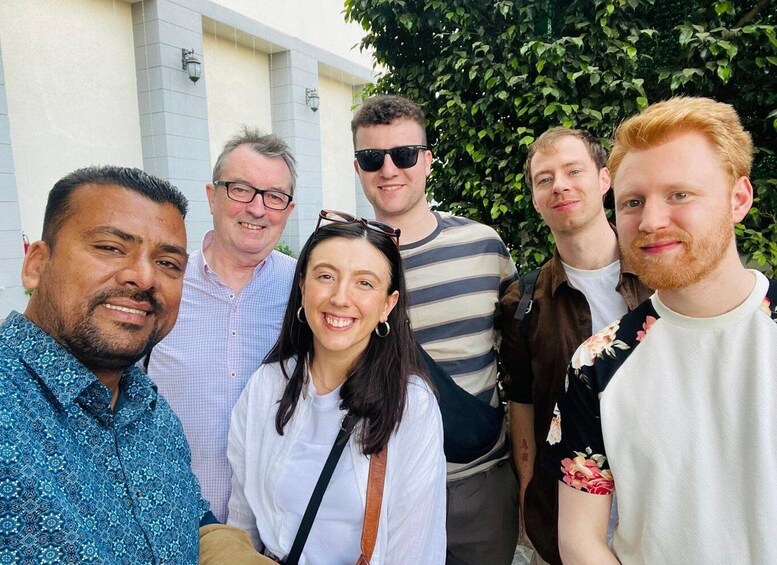 Un groupe de personnes se tient à l’extérieur, devant un bâtiment dont la façade est recouverte de carreaux et qui est bordé d’une haie verte. 3