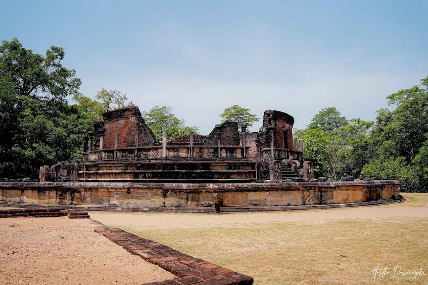 An ancient brick structure with a large central tower, surrounded by a low wall and trees. 5