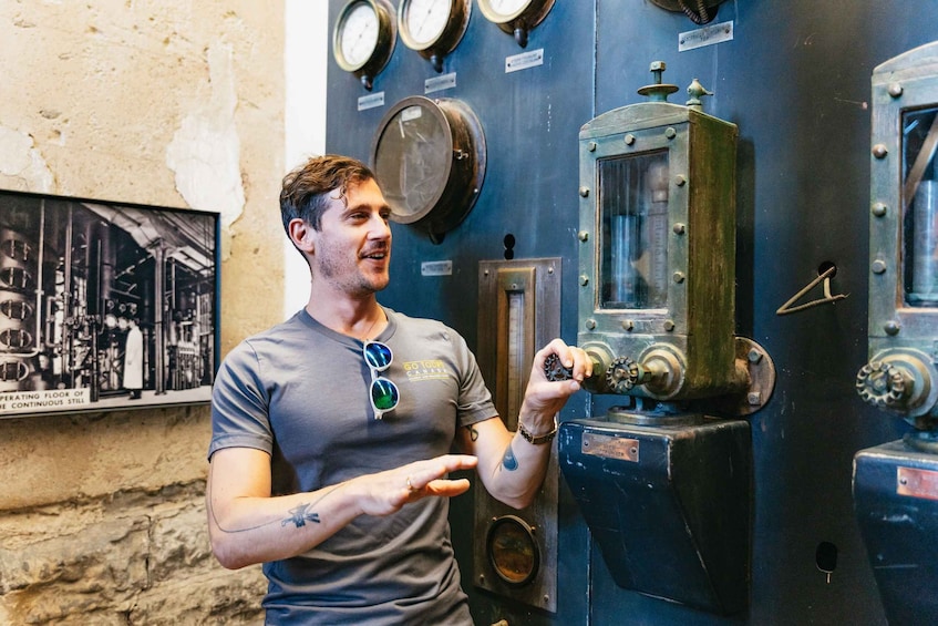 A man inspecting a mechanical device with gauges and dials, standing in front of a wall with industrial equipment and a poster. 1
