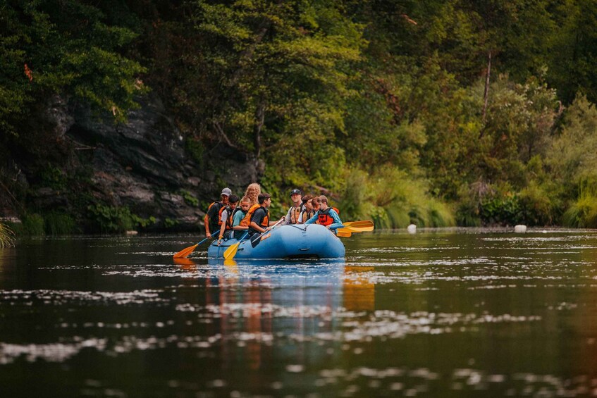 A group of people on a blue raft navigating a calm river surrounded by dense greenery. 5