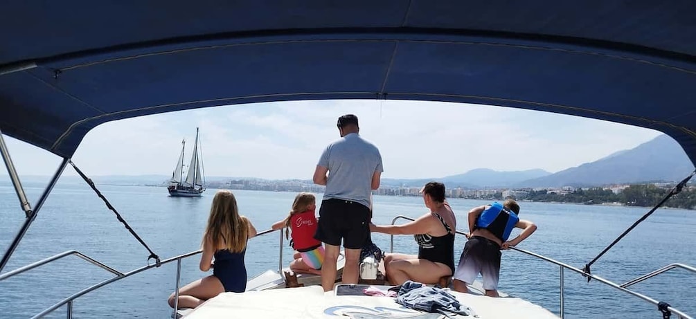 A group of people on a boat with a sailboat in the distance. 1