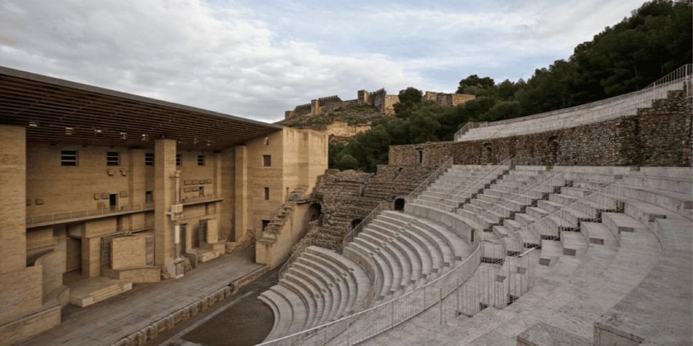 An ancient amphitheater with stone seating and a backdrop of historical ruins. 2