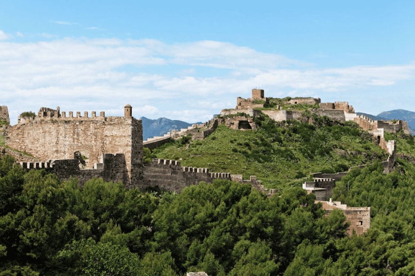 A historic stone fortress with battlements, surrounded by lush greenery and hills. 4