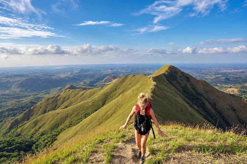 A hiker on a grassy hill with a view of a mountain range and a clear sky. 1
