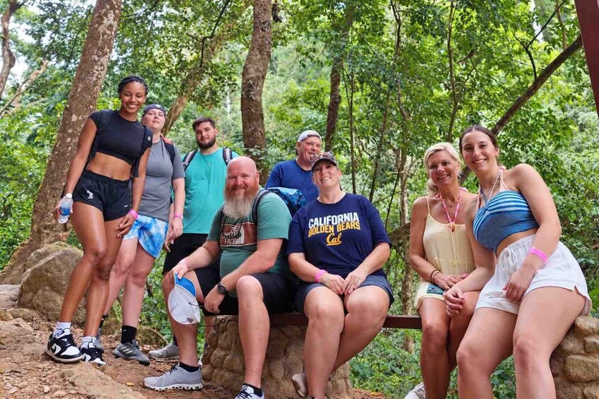 A group of people in a forested area with a stone bench. 5