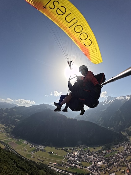 A paraglider with a yellow canopy flying over a mountainous landscape. 1