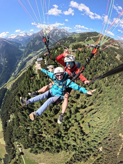 Two people paragliding over a mountainous landscape with trees and a ski lift in the background. 5
