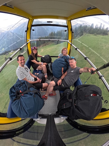 A group of people inside a yellow cable car with a mountainous landscape visible through the windows. 2