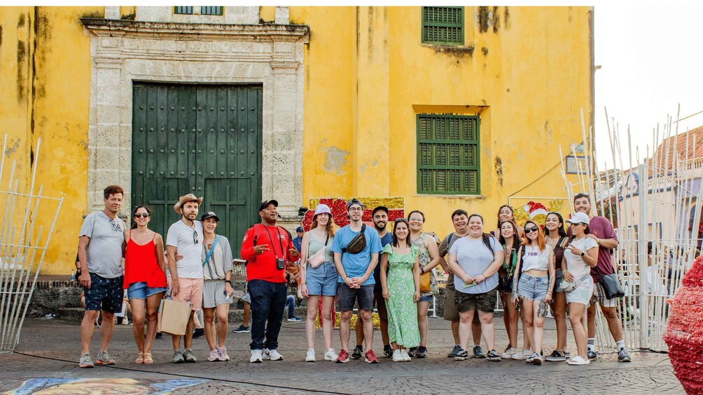 A group of people standing in front of a yellow building with a green door and window. 1