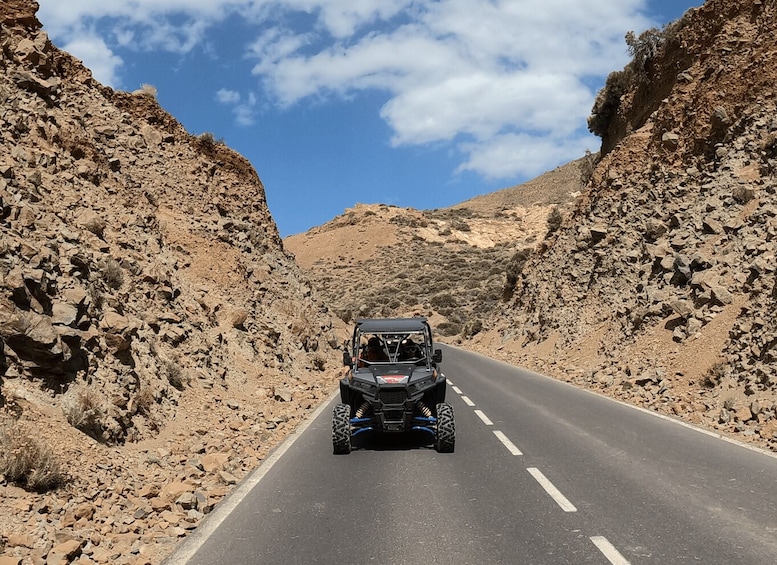 A vehicle driving on a paved road flanked by rocky terrain. 2
