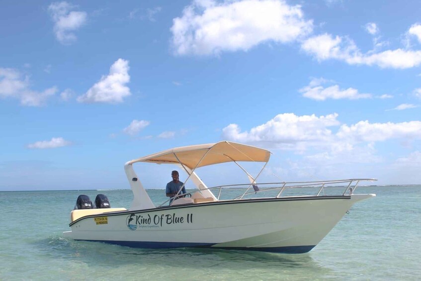 A white boat with a canopy labeled 'Kind Of Blue II' on a calm sea under a partly cloudy sky. 1