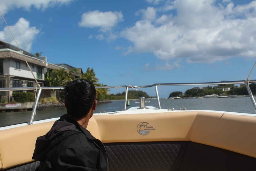 A boat with a logo on the side, a person in a black jacket, and a view of a body of water with buildings and trees in the background. 5