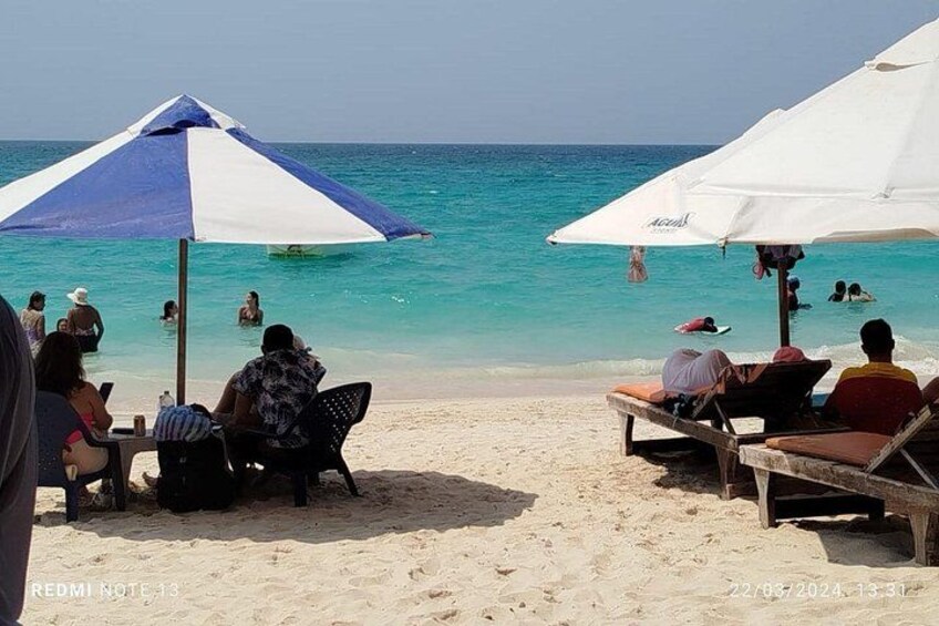 A beach with people relaxing under umbrellas, the ocean, and clear skies. 5