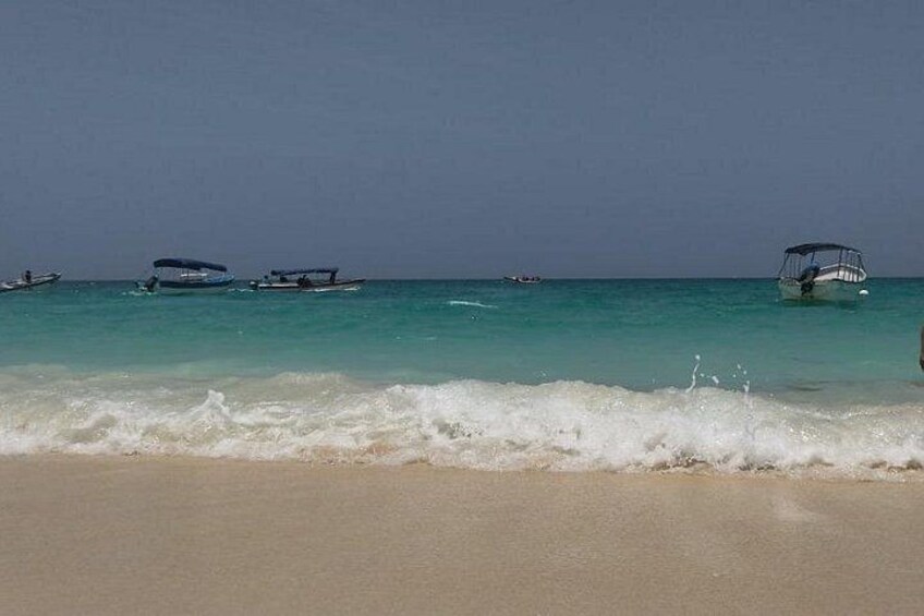 A beach with waves, a clear sky, and several boats in the water. 4