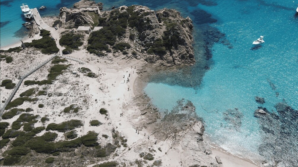 An aerial view of a coastal area with a beach, rocky outcrops, clear blue waters, and a lighthouse. 5