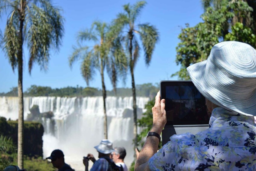 A person taking a photo of a waterfall with palm trees in the background. 1