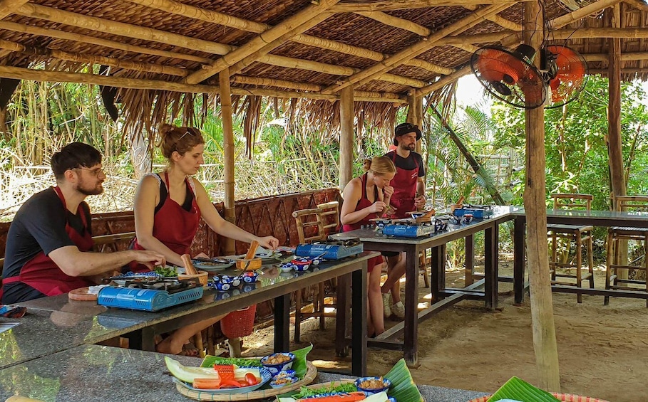 People preparing food outdoors under a thatched roof. 1