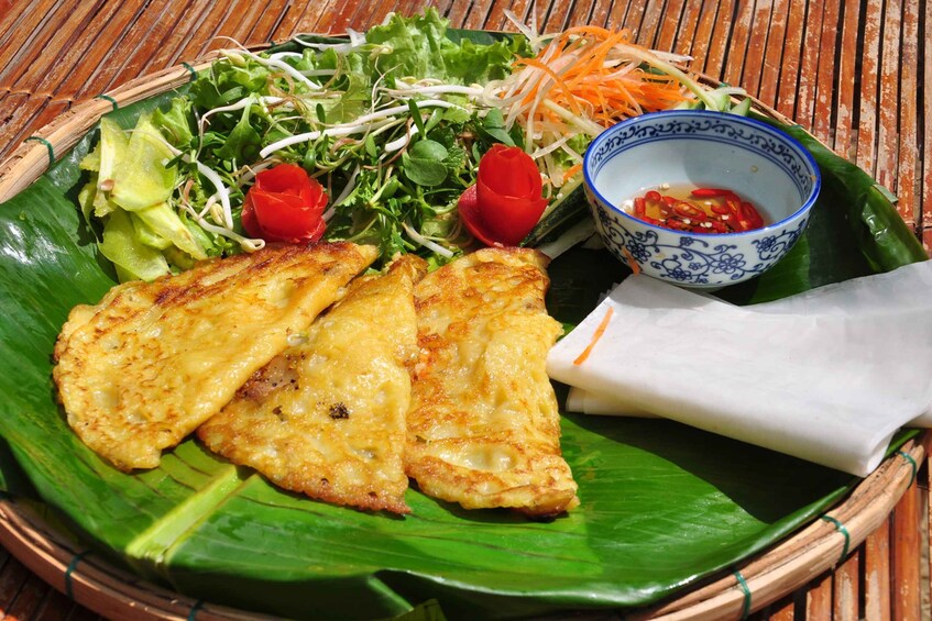 A plate of grilled chicken, a salad, and a bowl of dipping sauce on a green leaf. 5