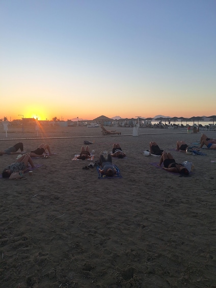 Ein Strand mit Menschen, die auf Matten liegen und sich sonnen, im Hintergrund sind Sonnenschirme zu sehen. 5