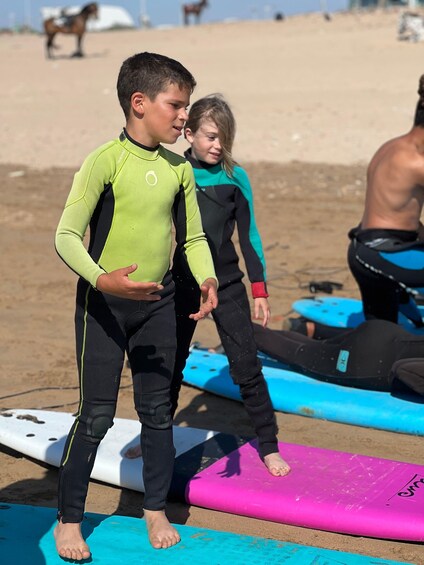 Dos personas con trajes de neopreno de pie en tablas de surf en una playa. 2