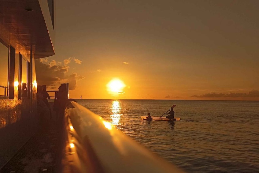 A sunset over the ocean with a pier and people paddling. 1