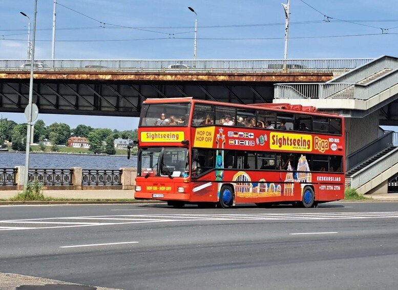 A red double-decker sightseeing bus with "Sightseeing Riga" and "Red Bus" advertisements, parked under a bridge. 5