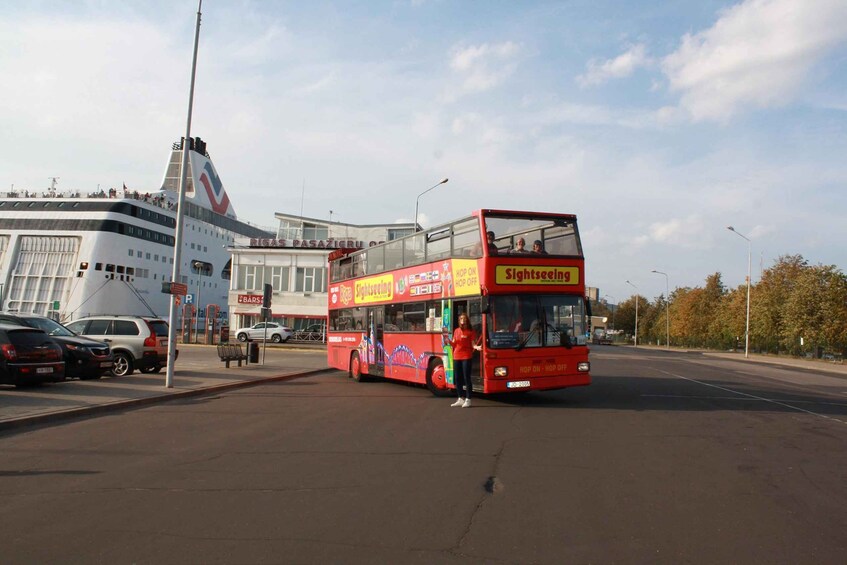 A red double-decker bus labeled "Sightseeing" parked on a street with cars and a building in the background. 1