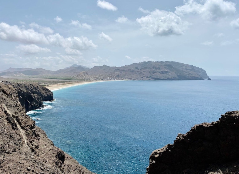 A coastal landscape with a clear blue sea, rocky cliffs, and distant mountains. 5