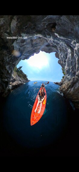 A kayaker in a red kayak entering a cave through a natural archway. 2