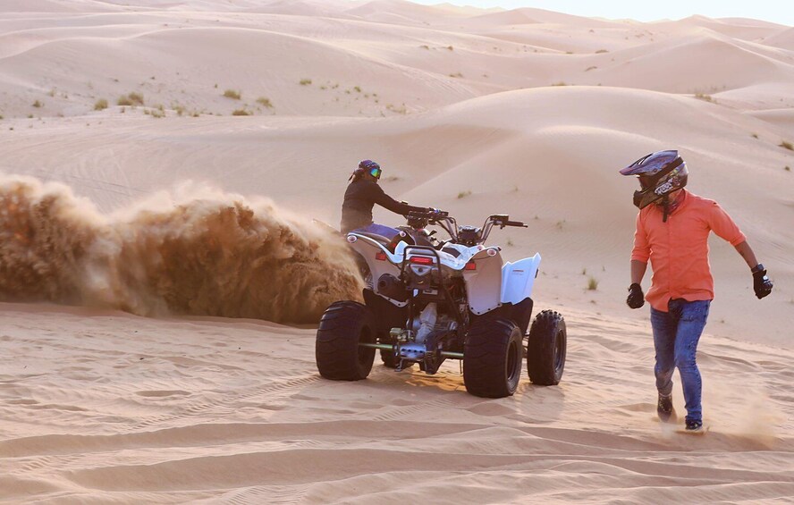A desert with sand dunes and two people on an ATV. 5