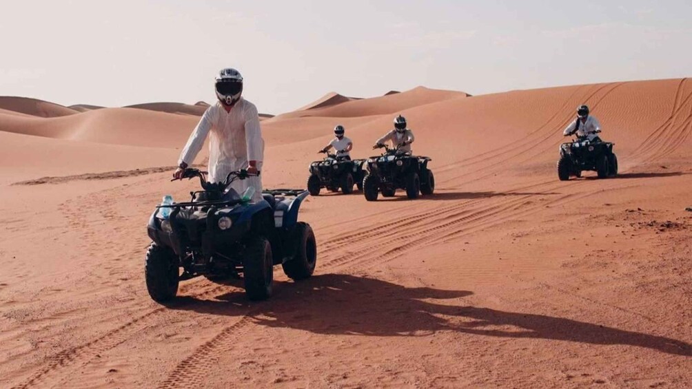 Four people riding ATVs on a desert dune. 3
