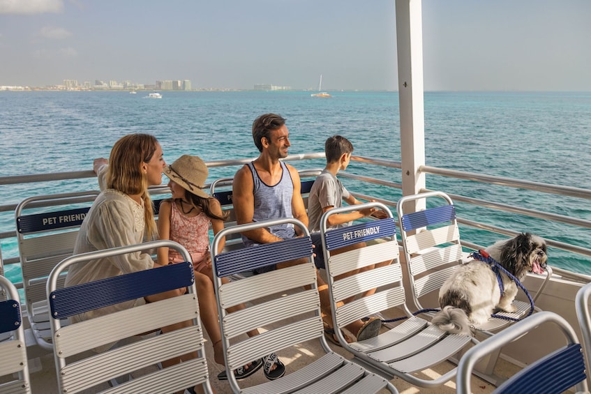 People on a boat with a dog, water, and a city skyline in the background. 1