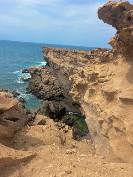 A coastal cliff with a narrow water passage and the ocean in the background. 5