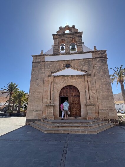 A historic church with a bell tower, arched entrance, and palm trees in the background. 3