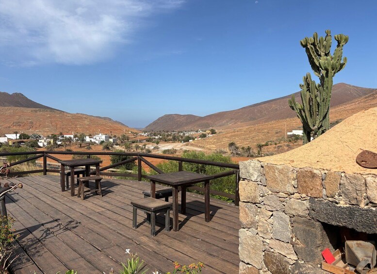 A wooden deck with tables and chairs overlooking a desert landscape with mountains and a small settlement. 2