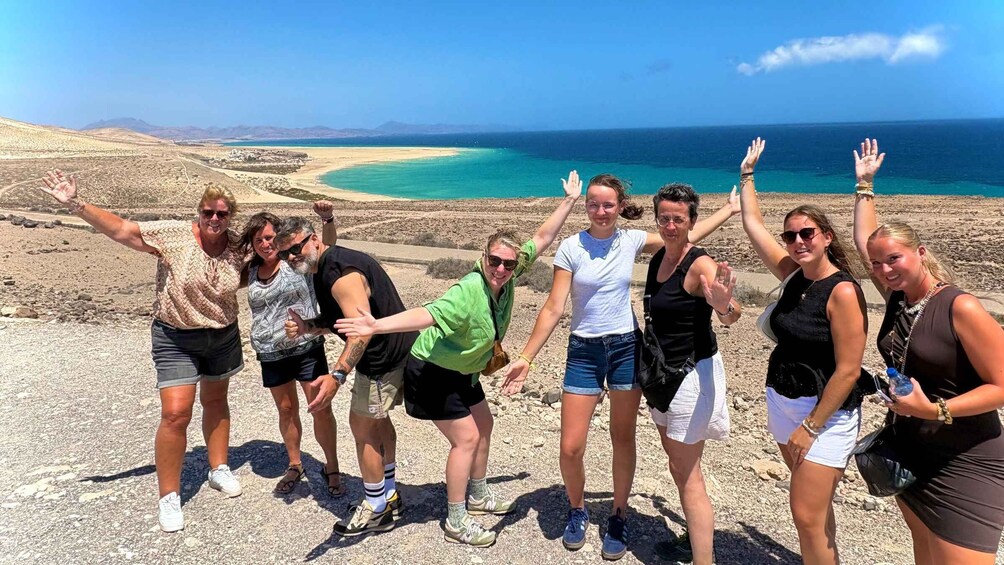 A group of people on a rocky outcrop with a beach and ocean in the background. 2