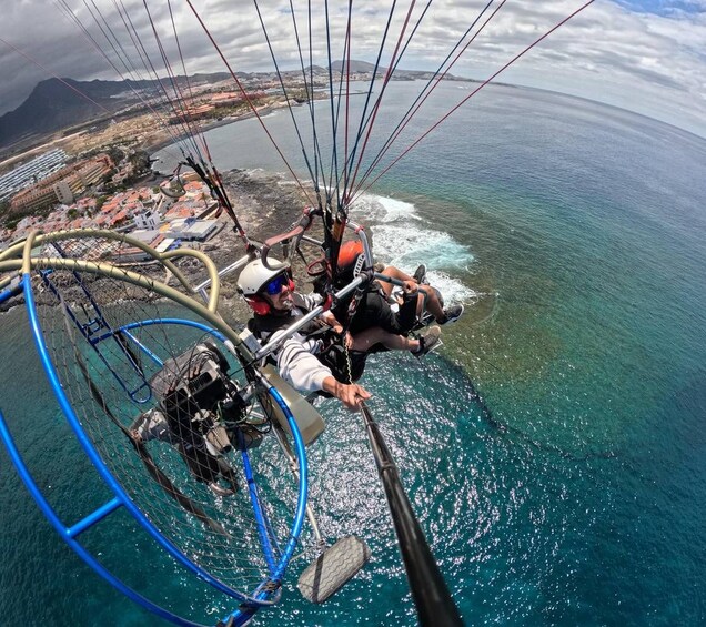 A paragliding scene with two individuals, a coastal landscape, and a mountainous backdrop. 2