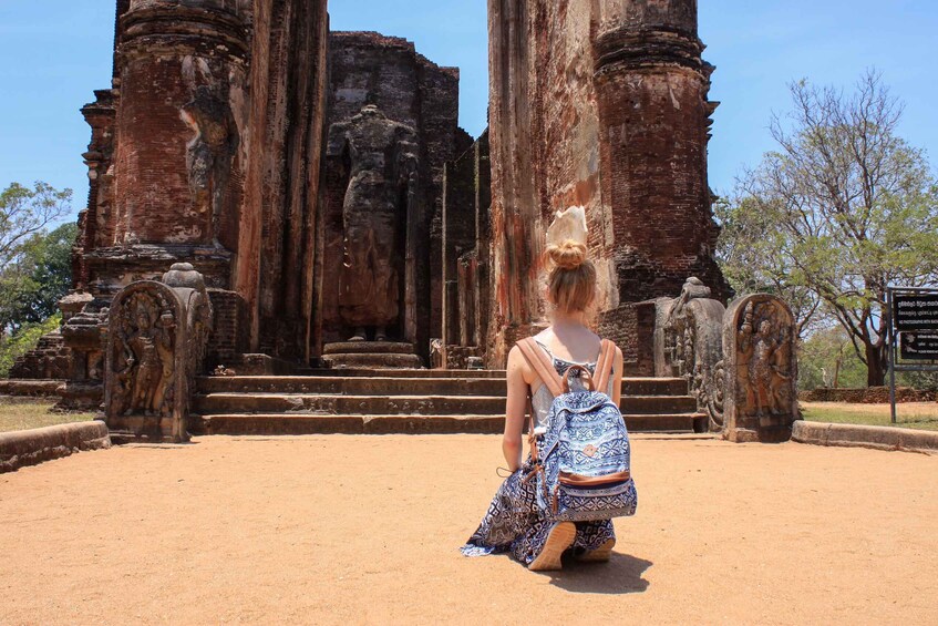 A person in a patterned dress kneeling in front of ancient stone structures. 5