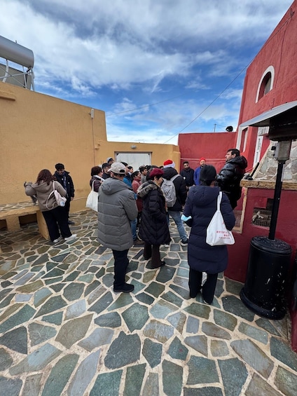 A group of people standing on a cobblestone street in front of a red building with a stone wall. 5