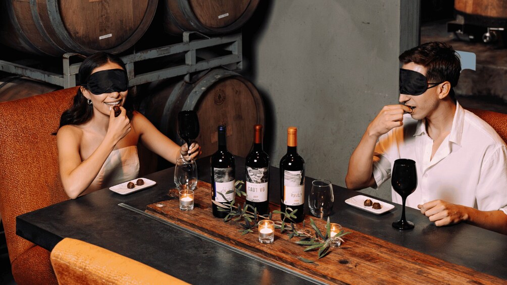 Deux personnes sont assises à une table, devant des bouteilles de vin, des verres et des assiettes remplies de nourriture. 5