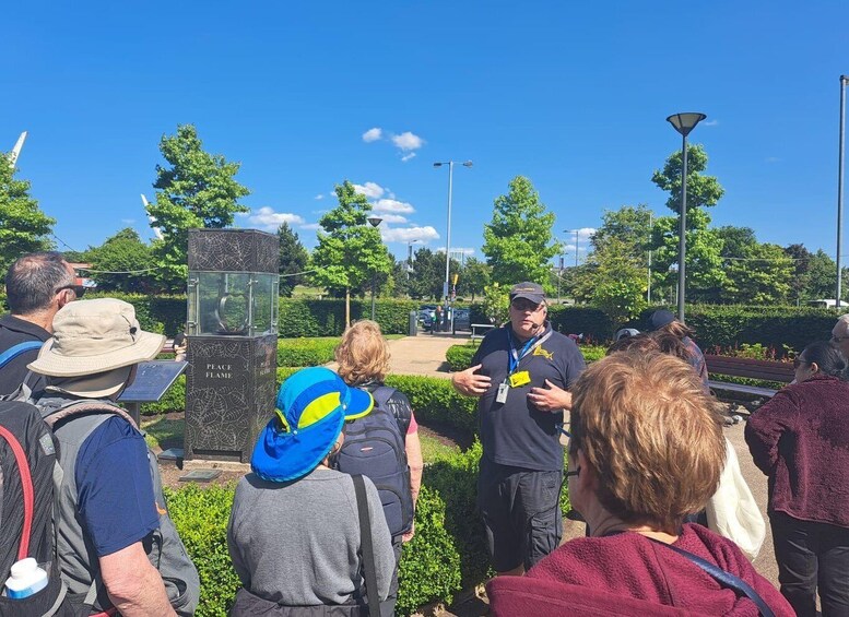 A group of people gathered around a monument with inscriptions, in a park with trees and a clear sky. 3