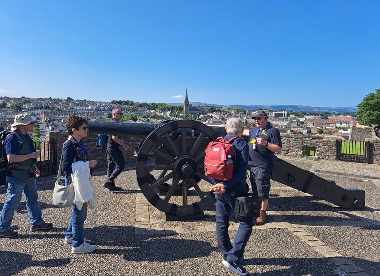 A group of people standing near a large cannon in a historical setting with a town in the background. 5