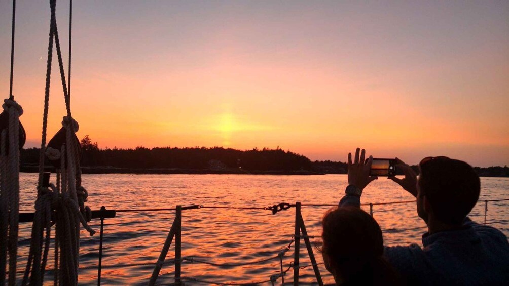 A person taking a photo of a sunset over a body of water with a boat and ropes in the foreground. 5