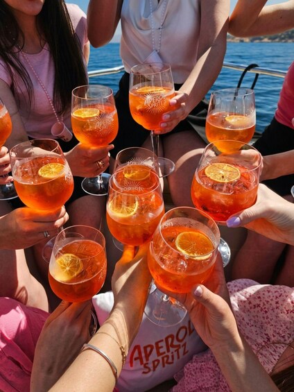 A group of people holding glasses of a red beverage with orange slices, on a boat. 4
