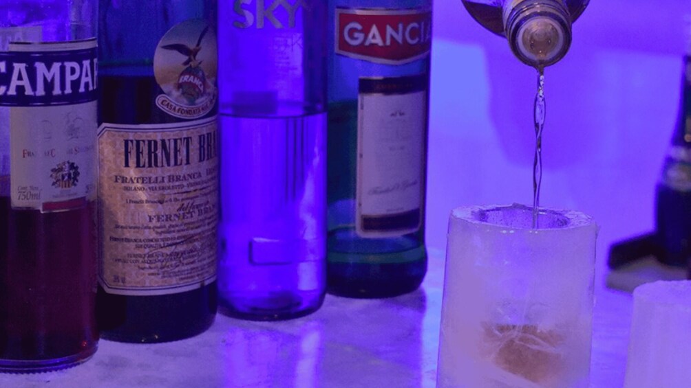 Variedad de botellas, incluyendo un Fernet Branca, sobre una barra mientras se sirve una bebida en un vaso. 2